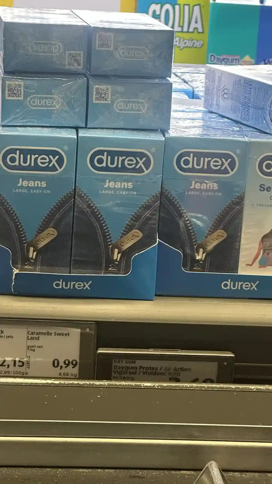 A shelf in a store displays stacks of blue Durex condom boxes labeled 'Jeans Large, Easy-On,' featuring an image of a zipper…