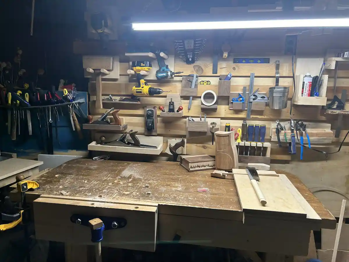 A well-organized woodworking workshop with a large wooden workbench in the foreground, covered in sawdust and holding a few…