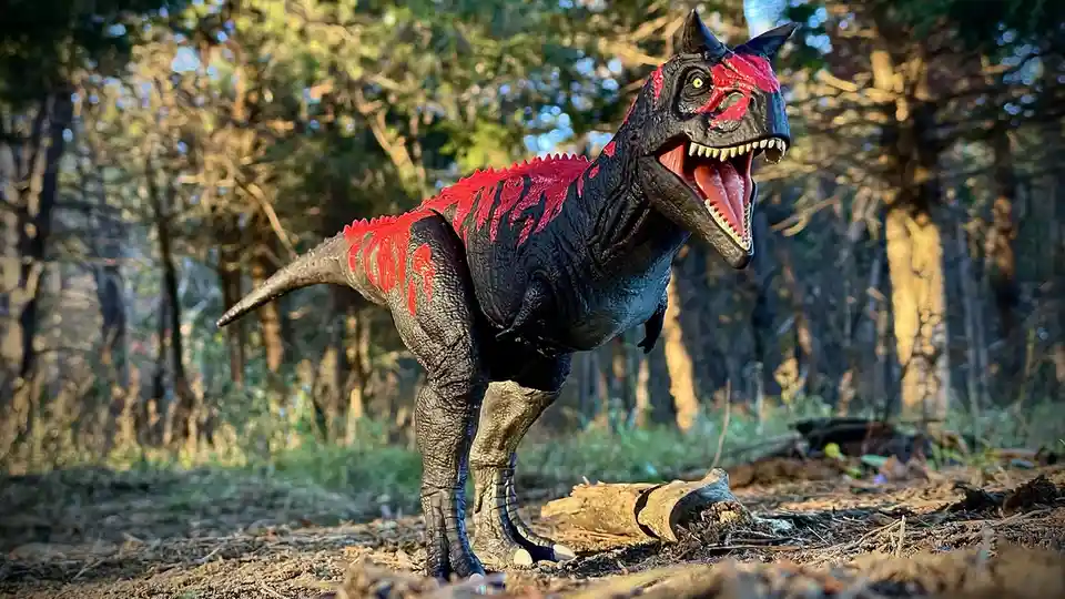 A black plastic dinosaur toy with red paint splatters on its back and head stands in a forest, mouth open as if roaring. The…