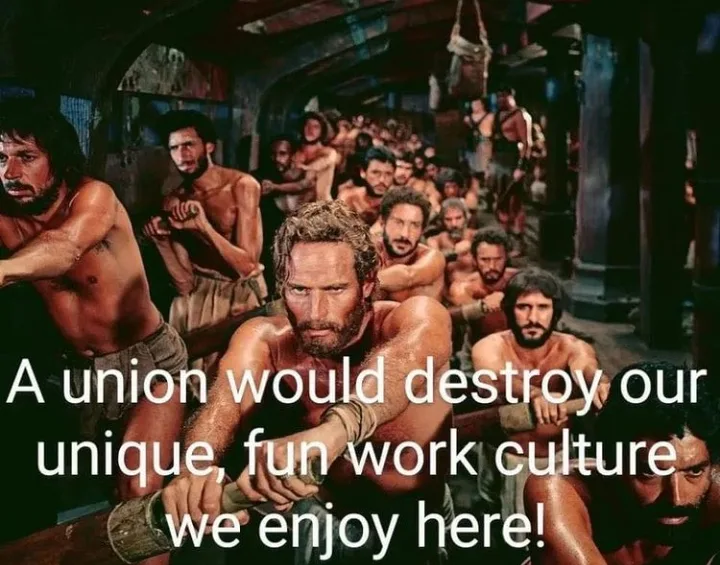 A group of shirtless, muscular men in a dimly lit, crowded, dungeon-like setting, all looking intensely forward. White text…