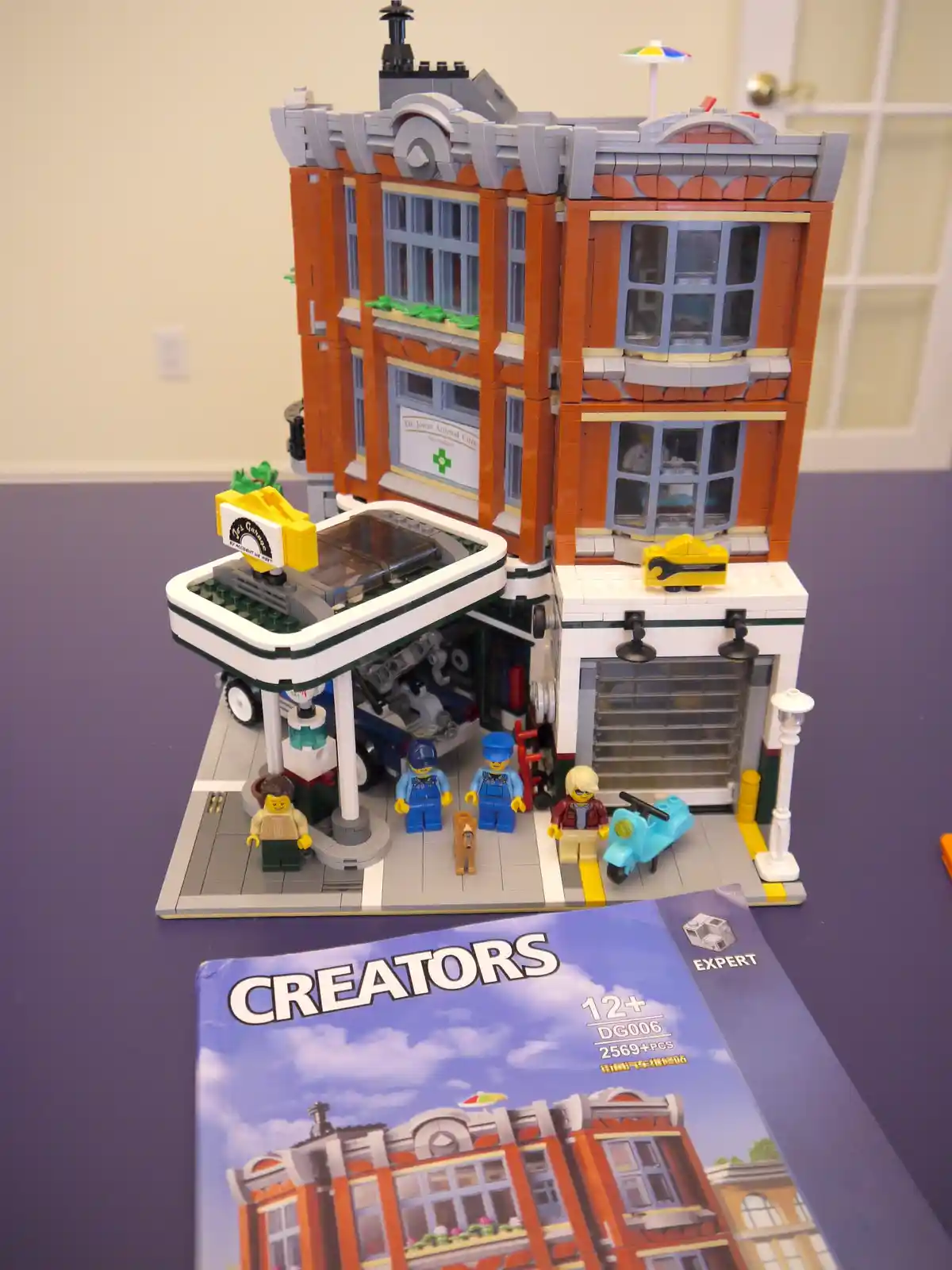 A completed LEGO Creator Expert set (DG006) depicting a detailed street-level auto repair shop with a multi-story building…