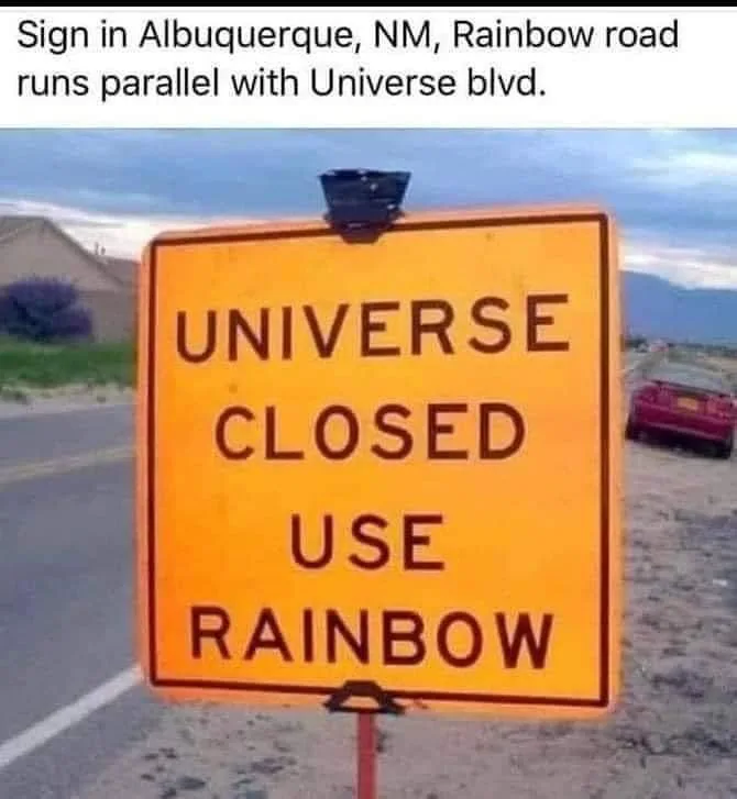 A yellow road sign with black text reads 'UNIVERSE CLOSED USE RAINBOW'. Above the image, text states 'Sign in Albuquerque…