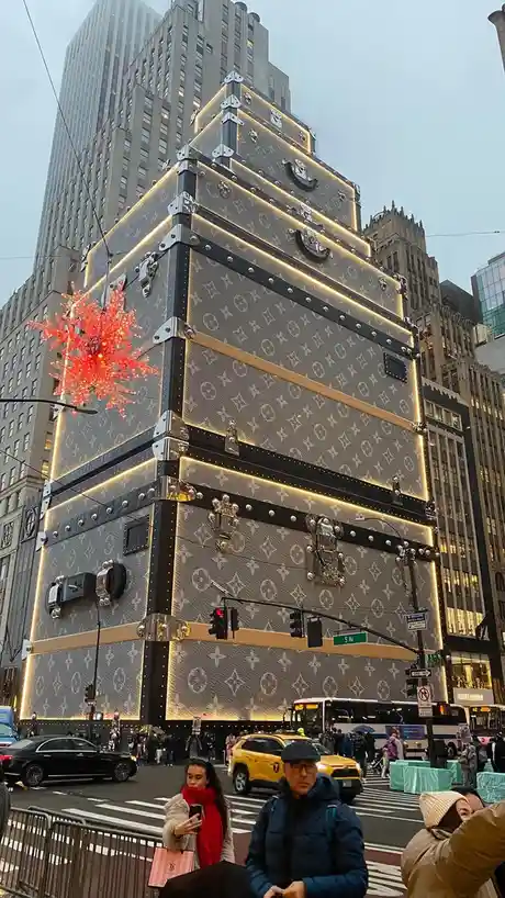 A towering, pyramid-shaped holiday display made of giant Louis Vuitton suitcases with glowing lights and a red snowflake…