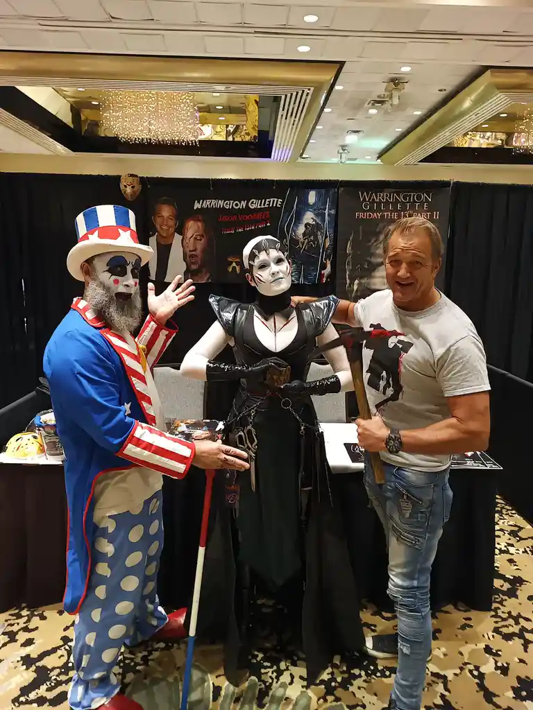 Three people pose together at a convention: one dressed as Uncle Sam with a cane, one in a black fantasy costume with a…