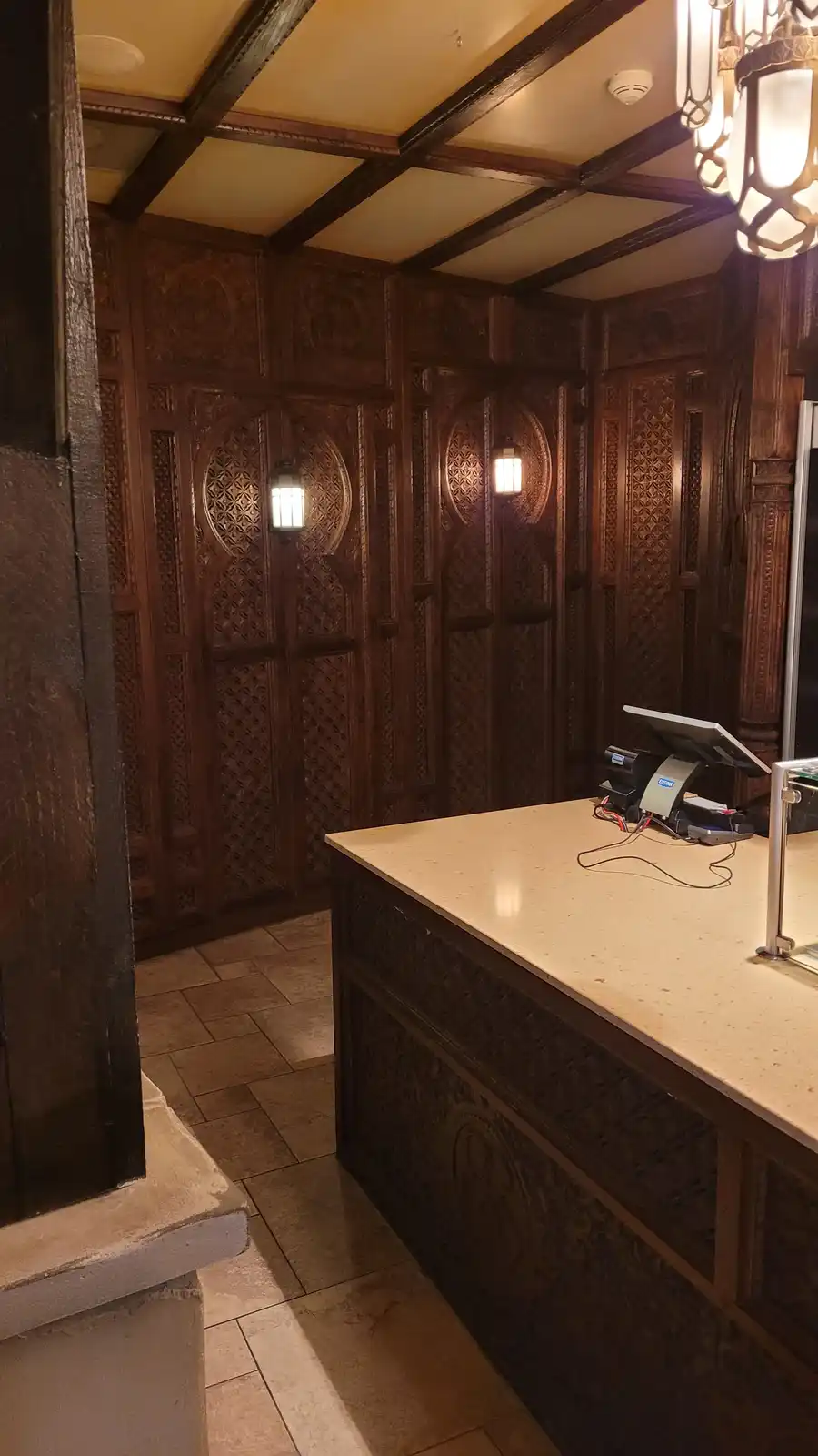 The image shows an ornate, wood-paneled hotel lobby with intricate carvings on the walls and ceiling beams, featuring warm…