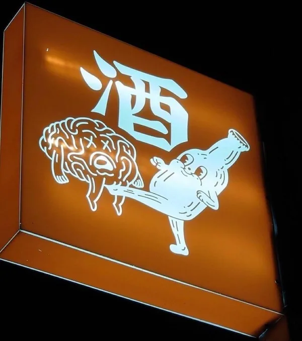 An illuminated orange sign at night features a large white Chinese character '酒' (jiǔ, meaning alcohol) above a cartoonish…