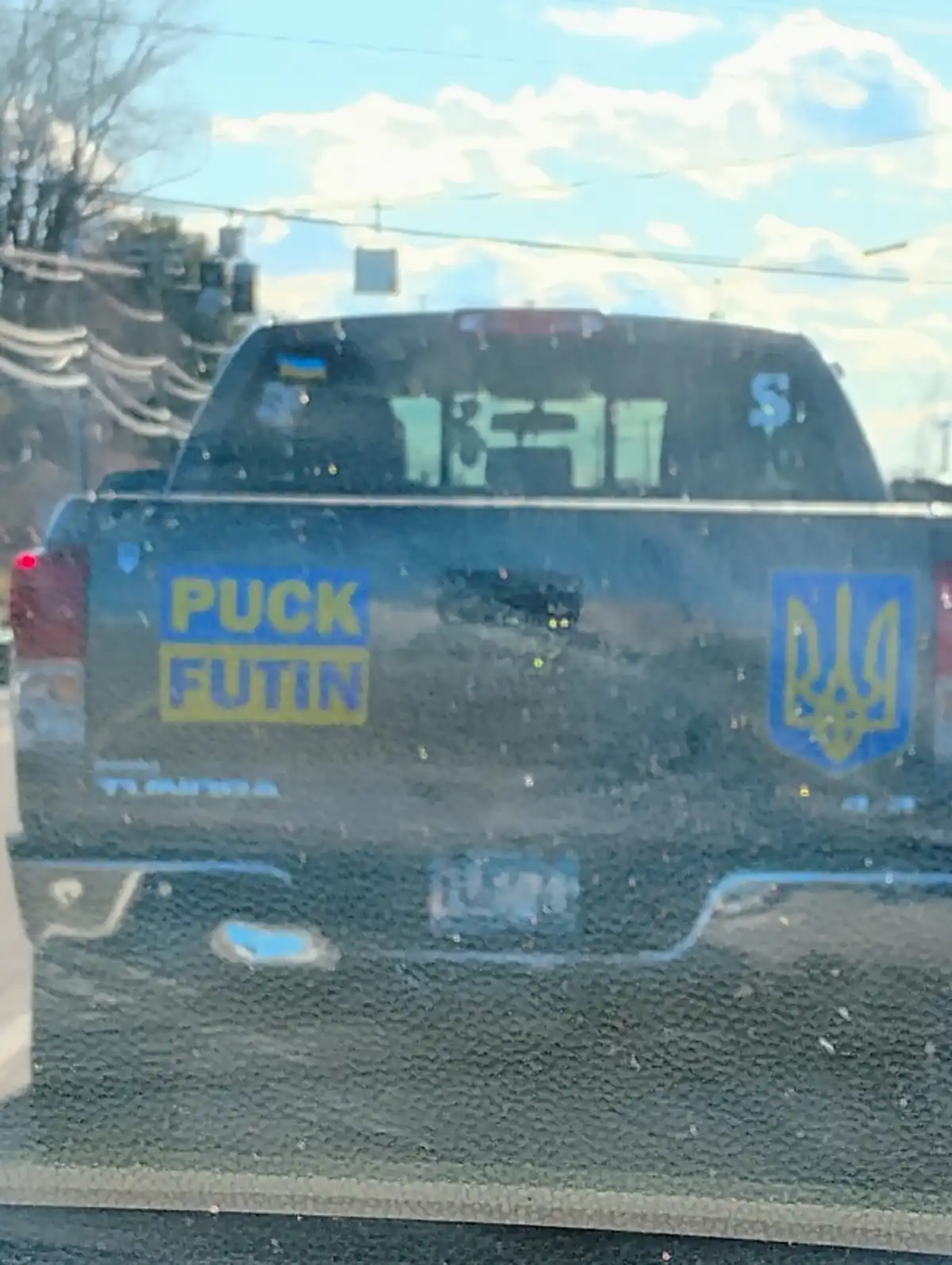 The rear of a dark pickup truck is shown, viewed through a slightly dirty window. On the truck bed, a blue and yellow…