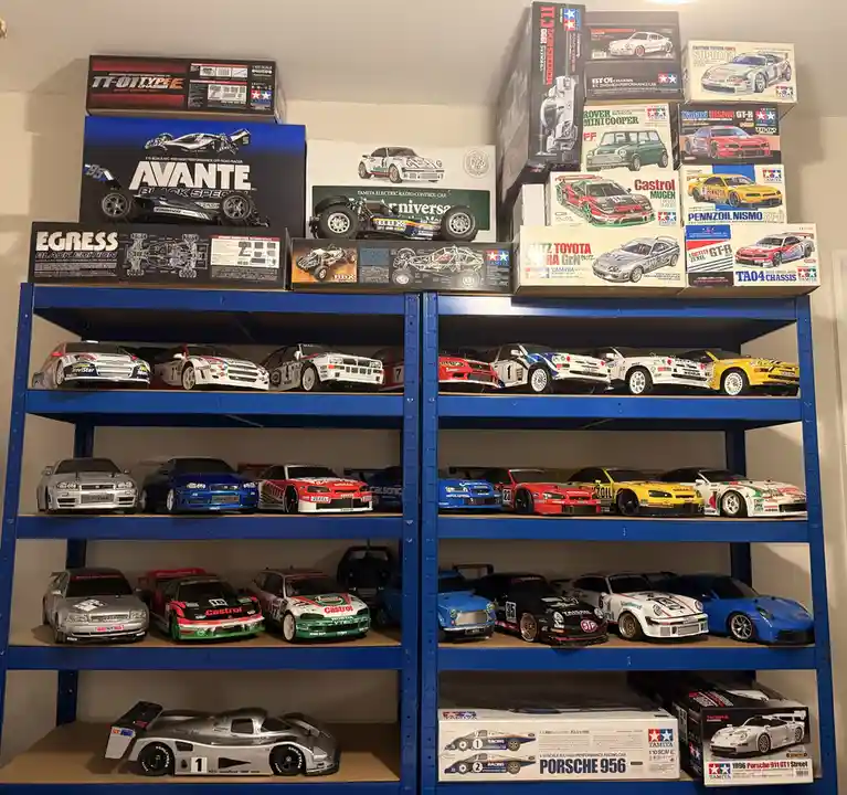 A large blue metal shelving unit is filled with numerous radio-controlled model cars, both assembled and in their original…