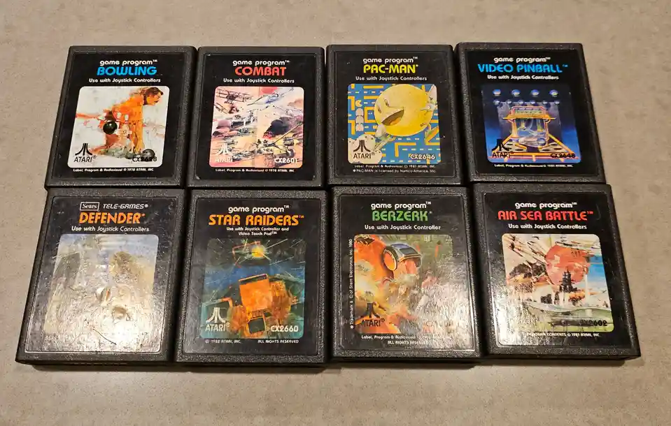 Eight Atari 2600 game cartridges are arranged in two rows on a gray surface. The visible titles include Bowling, Combat…