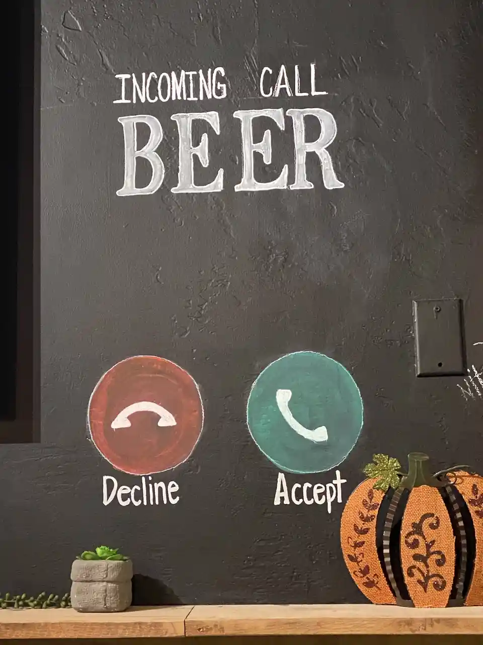 A chalkboard wall displays a mock phone call interface with 'INCOMING CALL BEER' written in large white letters. Below are…