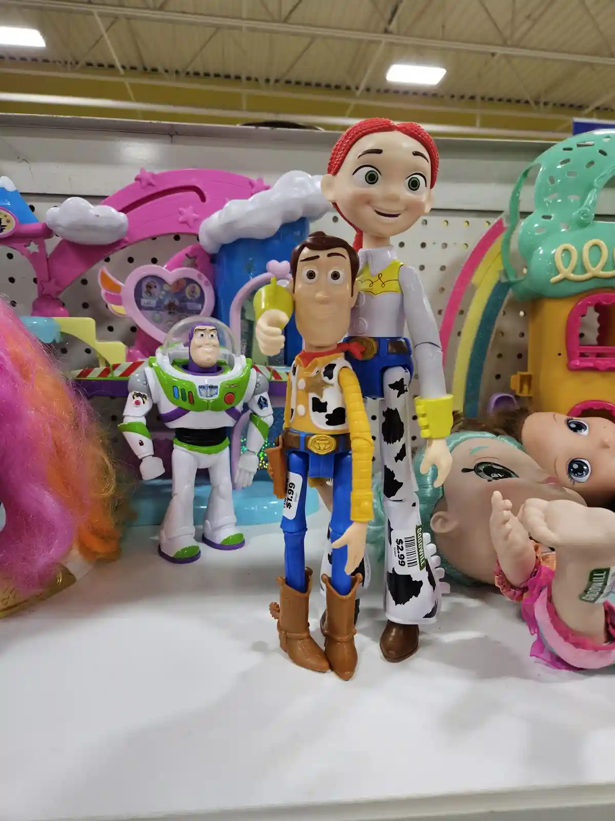 Three Toy Story action figures—Buzz Lightyear, Woody, and Jessie—are displayed on a store shelf with price tags visible…