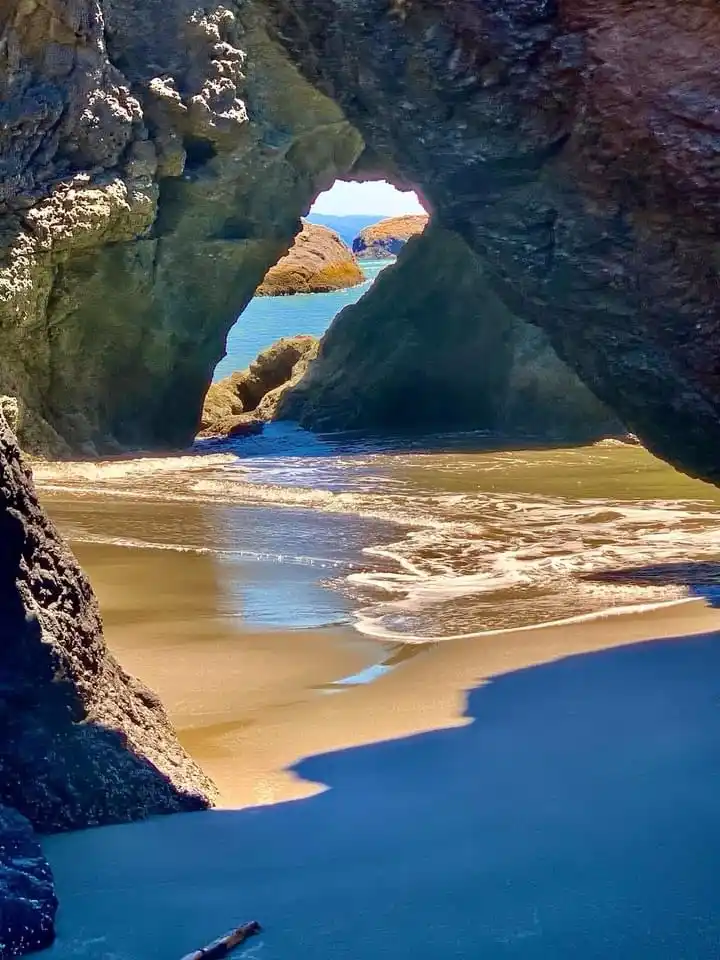 A scenic photo of a natural rock archway framing a beach and ocean, with waves lapping at the sand. Overlaid text reads 'i'm…