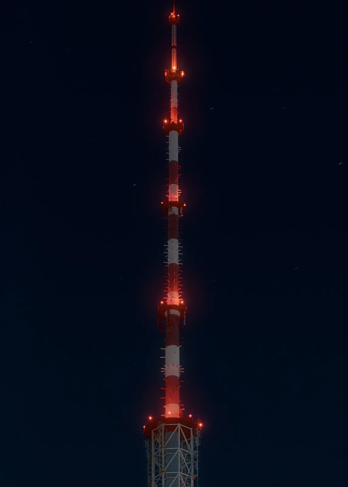A tall, red-and-white striped communication tower stands against a dark night sky, illuminated by red lights at various…