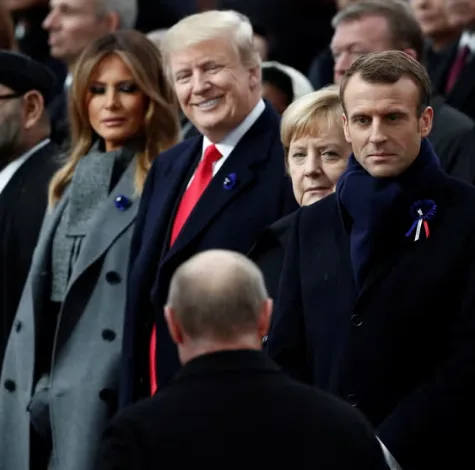 A photo of Donald Trump, Melania Trump, Angela Merkel, and Emmanuel Macron at a public event, with Trump smiling broadly…