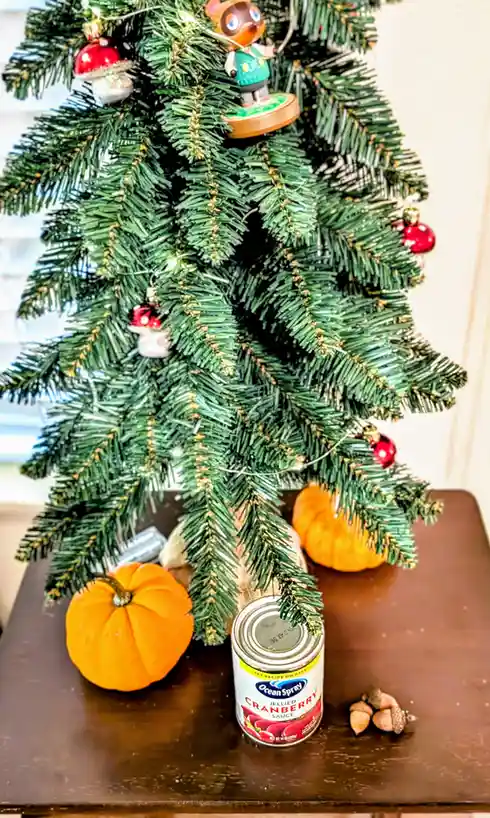 A decorated artificial Christmas tree with holiday ornaments stands on a table next to two small pumpkins, a can of Ocean…
