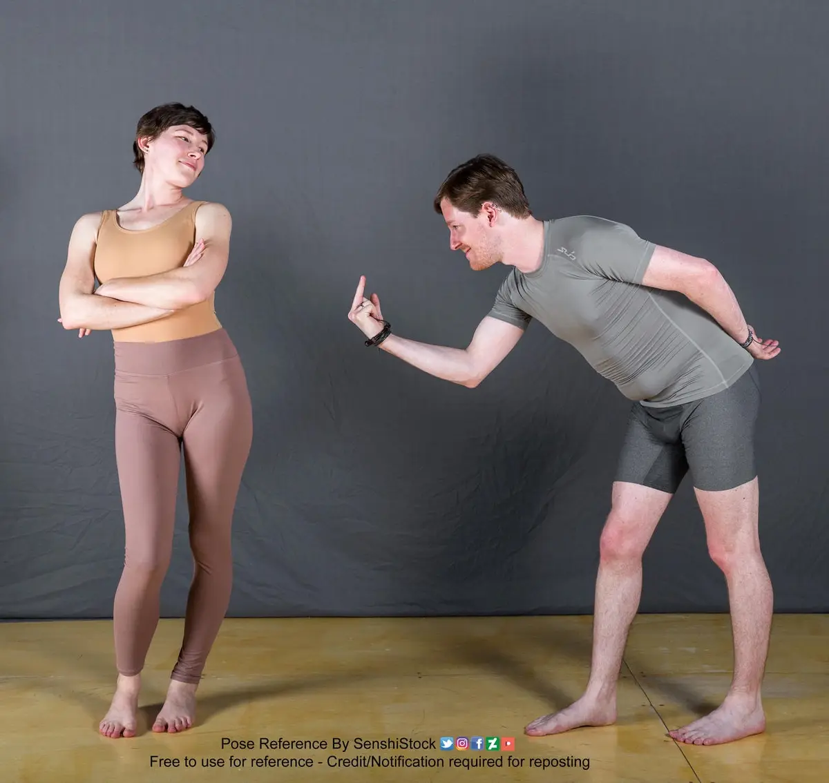 A man in grey athletic wear leans forward, pointing his finger at a woman in beige workout clothes who stands with her arms…