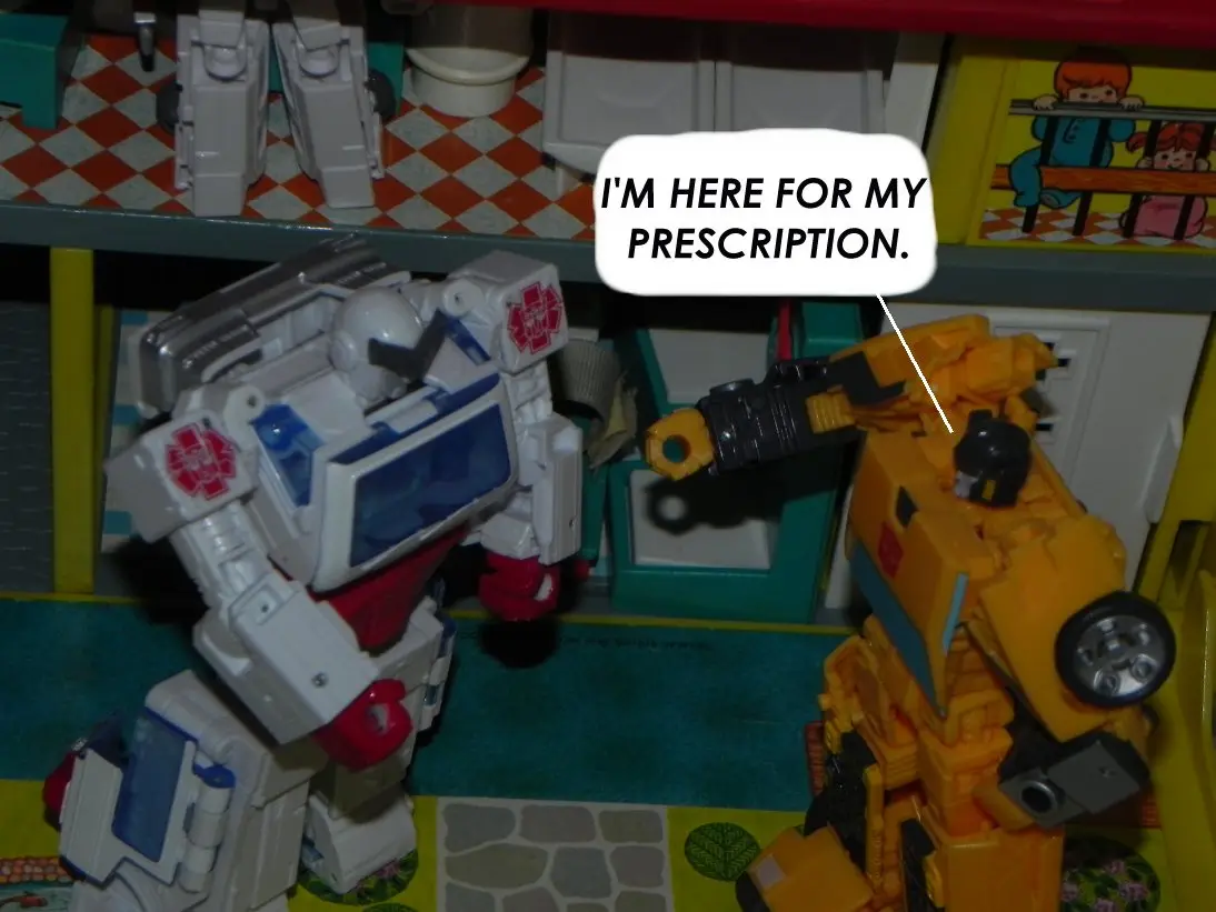 Two Transformers toys, one white and blue with a medical symbol, and one yellow and black, are positioned in a toy kitchen…