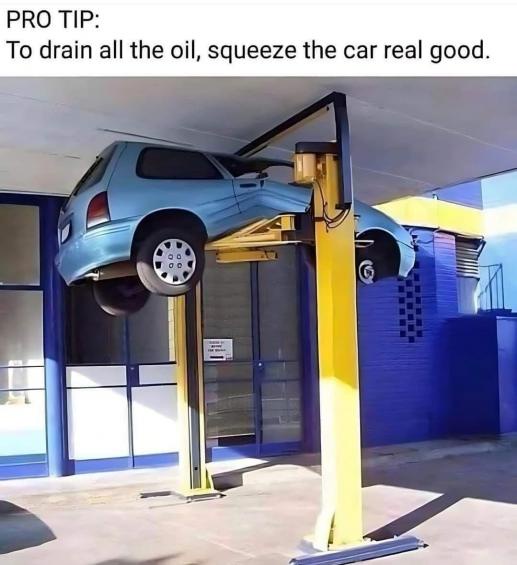 A light blue car is suspended by a yellow hydraulic lift in a garage, visibly squeezed and distorted as if being compressed…