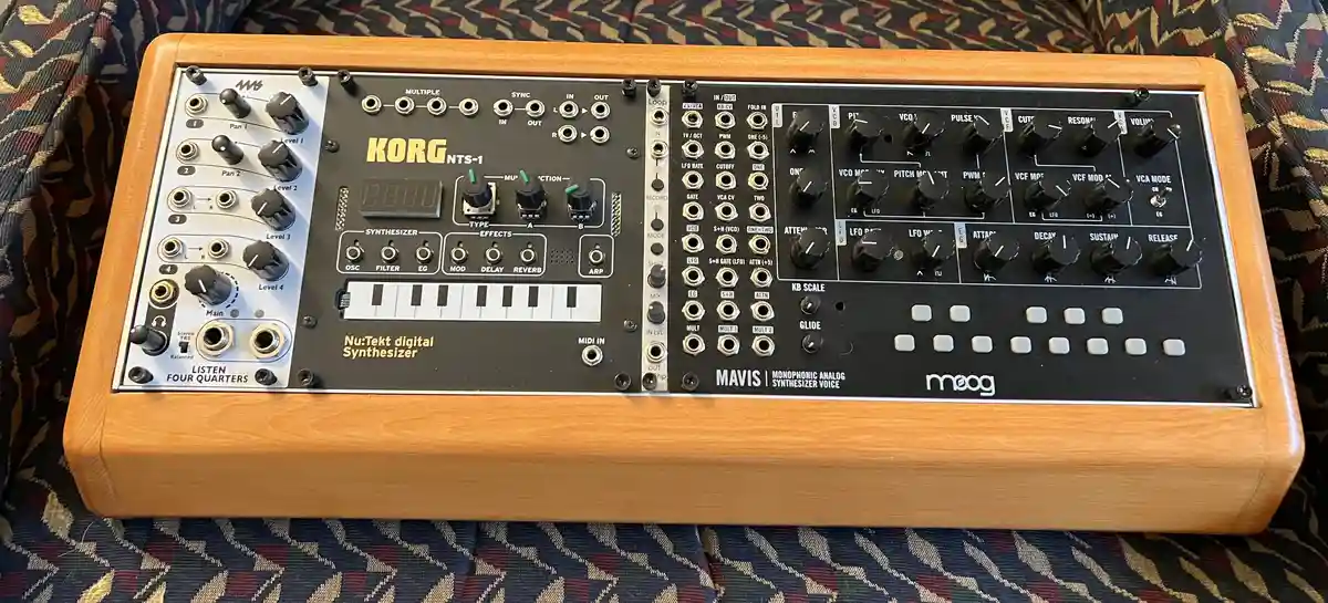 A Korg NTS-1 synthesizer with a wooden case is shown, featuring a small keyboard, numerous knobs, and jacks. The left side…