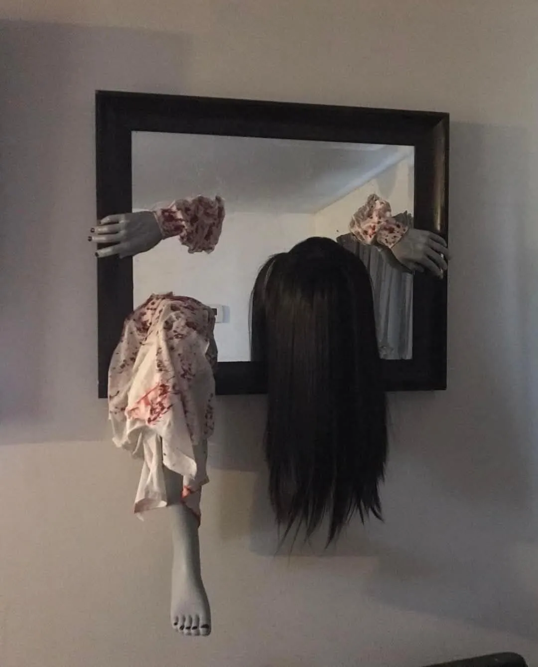 A horror-themed photo shows a mannequin torso with a long black wig and blood-stained clothing, seemingly emerging from a…