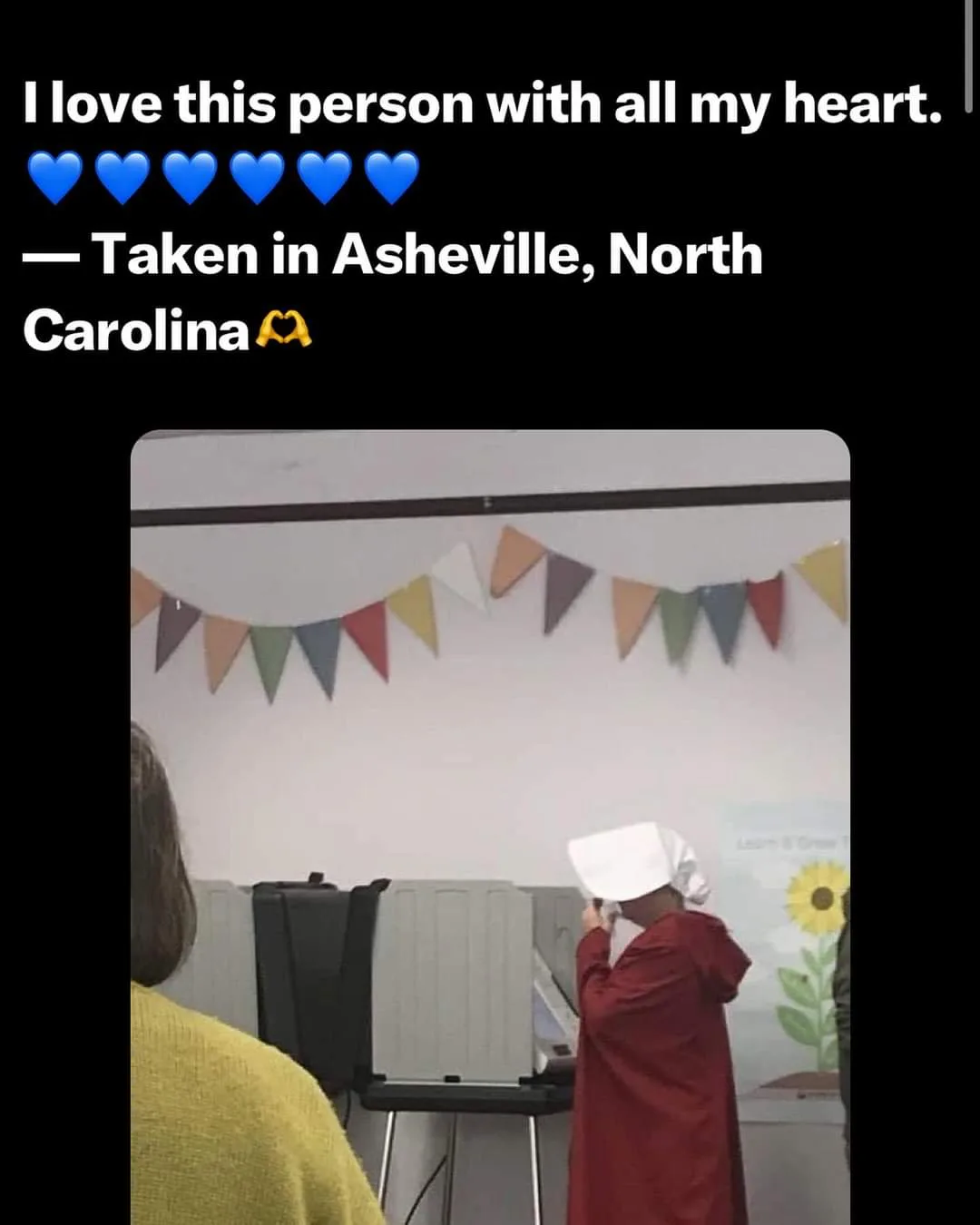 A person wearing a red robe and white bonnet, resembling a character from 'The Handmaid's Tale,' stands at a voting booth in…