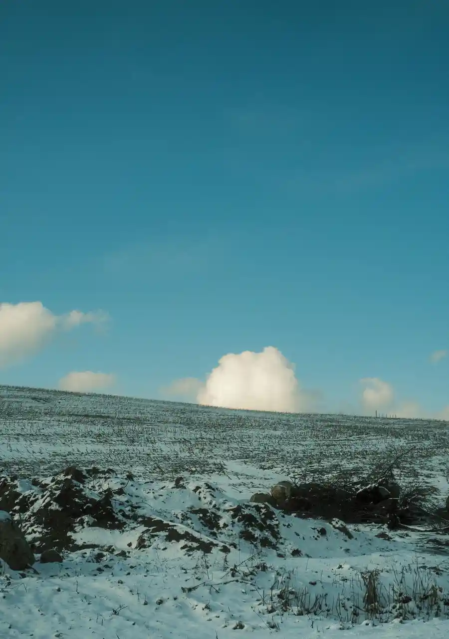 A snowy, barren hillside under a vast blue sky with scattered white clouds, overlaid with the text 'i'm not lazy, i'm in…