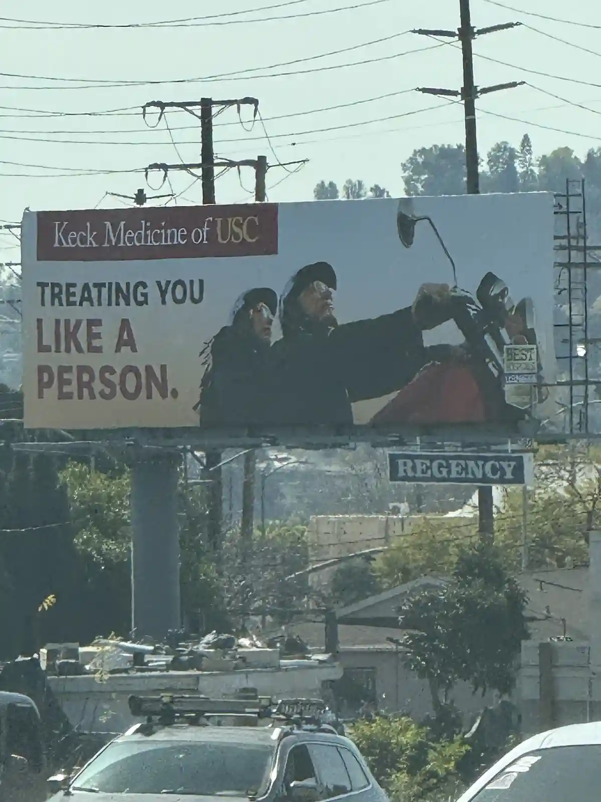 A billboard for Keck Medicine of USC features a photo of several people in dark clothing and hats, seemingly in a tense or…