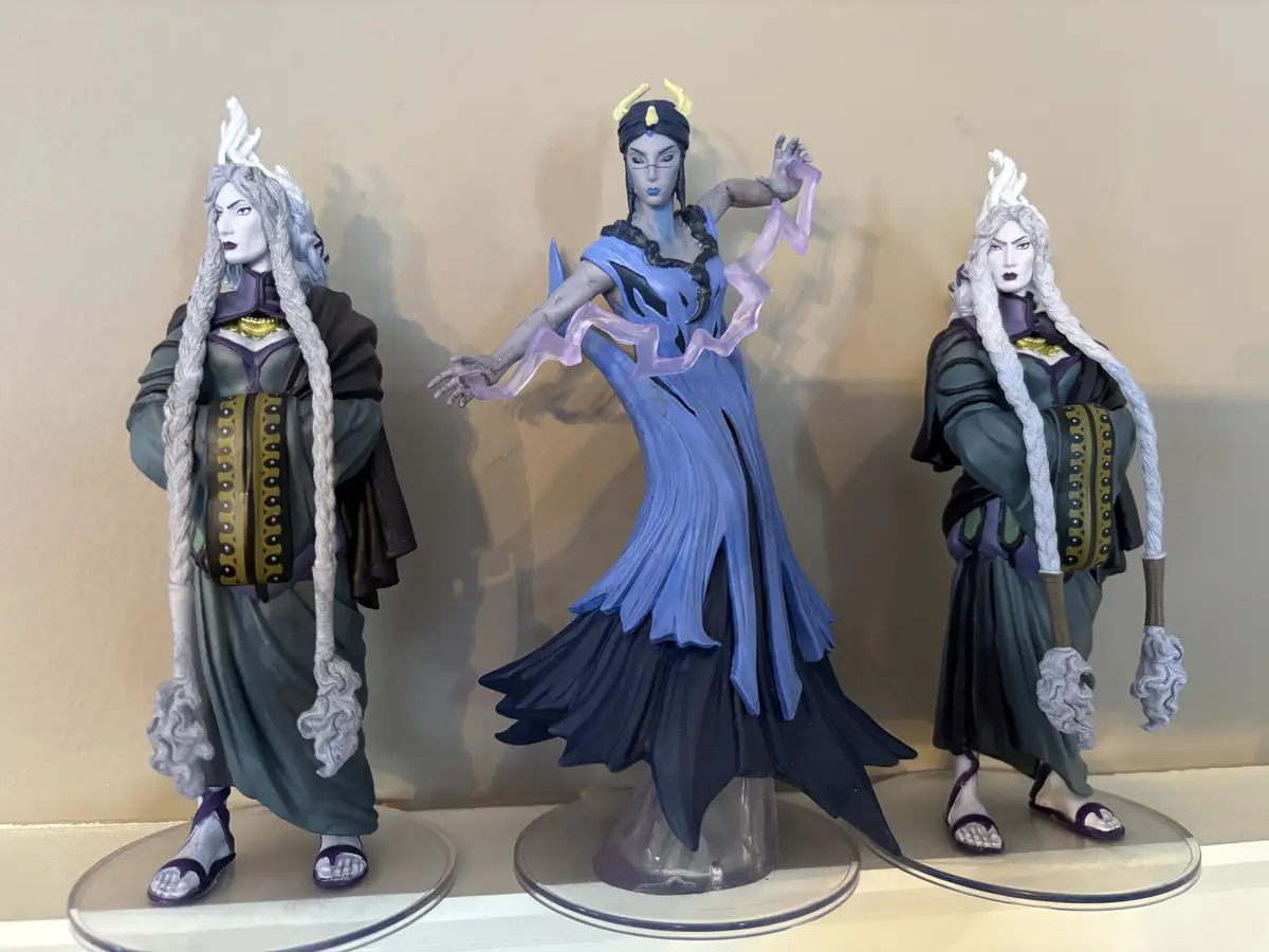 Three figurines of the character Sif from Marvel are displayed side by side on clear circular bases against a beige wall…