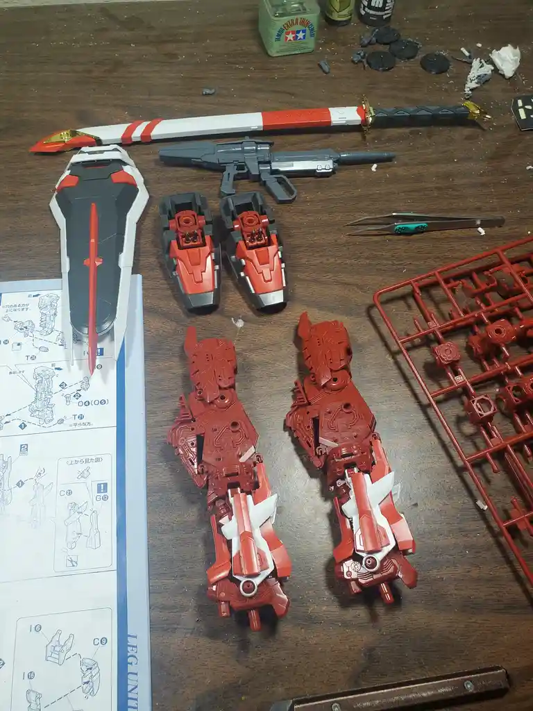 A wooden table displays a partially assembled red and white robot kit with its legs detached and lying separately, alongside…