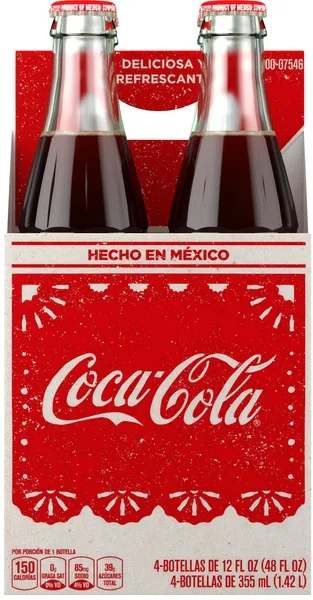 A six-pack of Coca-Cola glass bottles with red and white packaging. The label prominently displays 'HECHO EN MÉXICO' (Made…