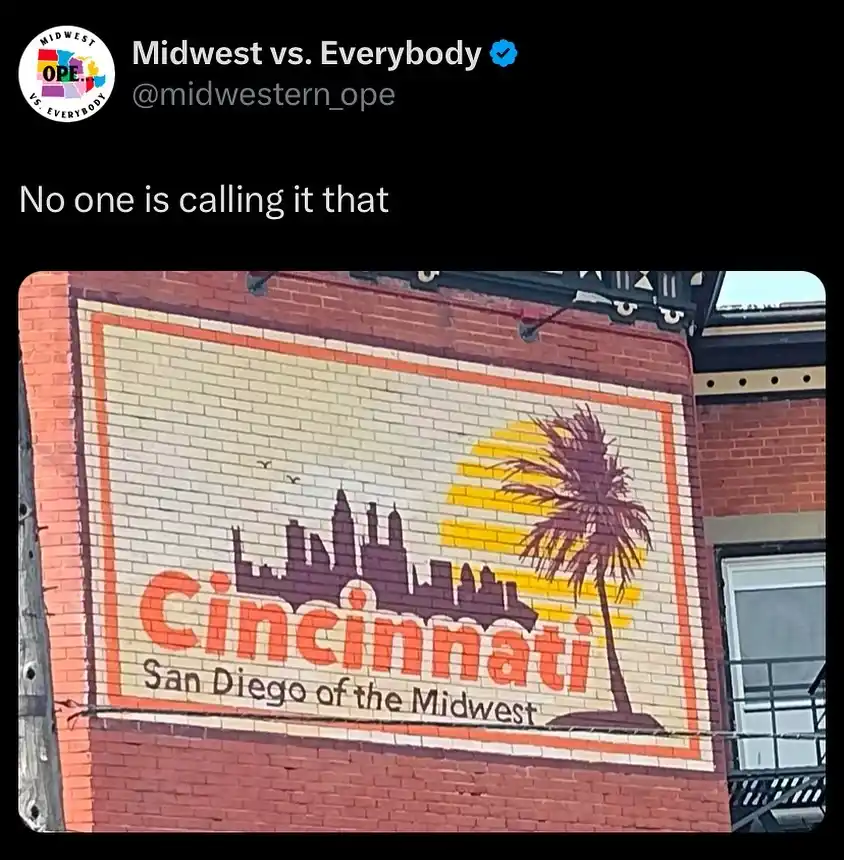 A brick wall mural depicts a city skyline with a palm tree and sunset, labeled 'Cincinnati San Diego of the Midwest'. The…