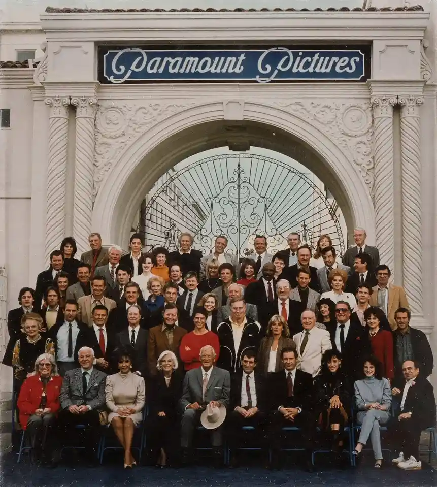 A large group photo of numerous actors, directors, and studio executives posing in front of the iconic Paramount Pictures…