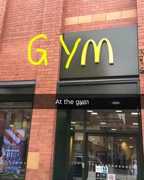 A brick building with a black sign that reads 'GYM' in yellow letters, styled to mimic the McDonald's logo. Below the sign…