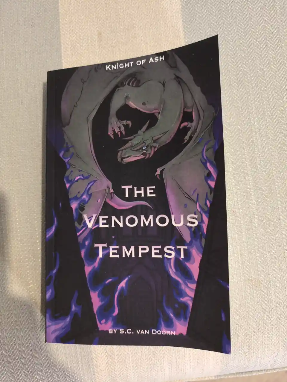 A book titled 'The Venomous Tempest' by S.C. Van Doorn, part of the 'Knight of Ash' series, features a menacing green dragon…