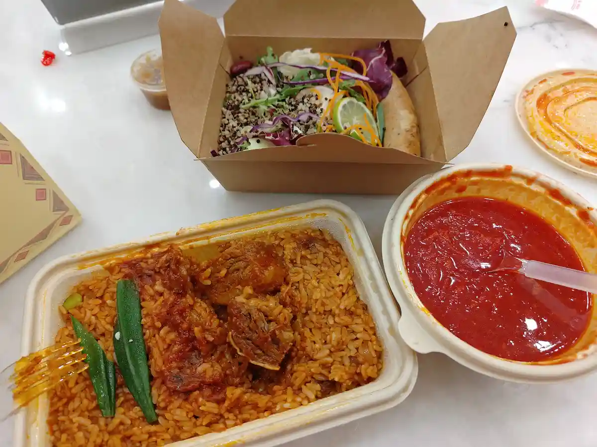 A photo shows two takeout containers on a white table: one holds a colorful salad with quinoa, vegetables, and a lime wedge…