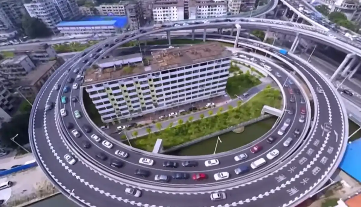 an aerial view shows a multi-lane highway forming a large circular loop around a multi-story building, with cars moving in…