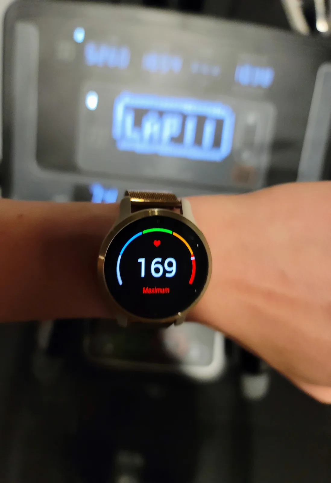 A close-up of a person's wrist wearing a smartwatch displaying a heart rate of 169 with the word 'Maximum' below it, while…