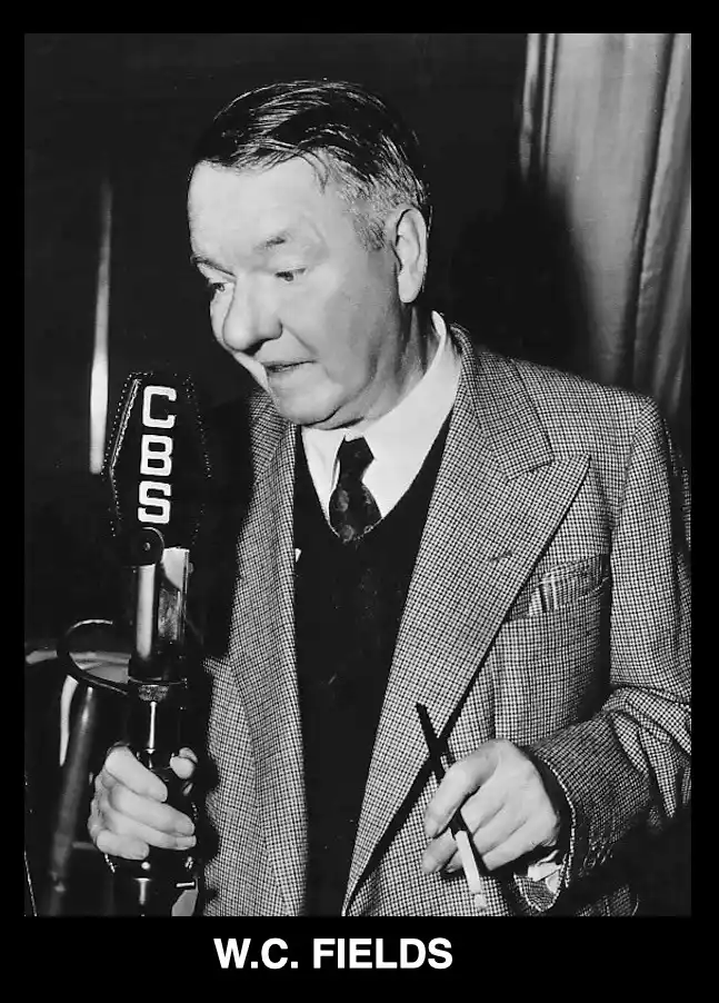 A black-and-white photograph shows actor W.C. Fields holding a vintage CBS microphone in one hand and a cigarette in the…