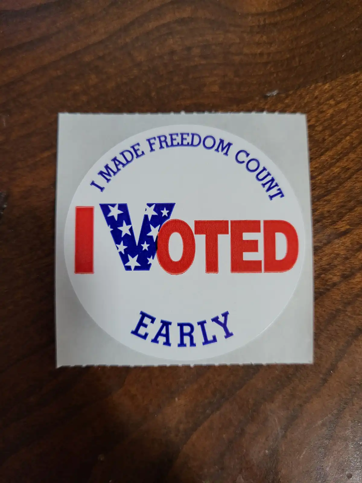 A circular white sticker with red and blue text sits on a wooden surface. The top arc reads 'I MADE FREEDOM COUNT' in blue…