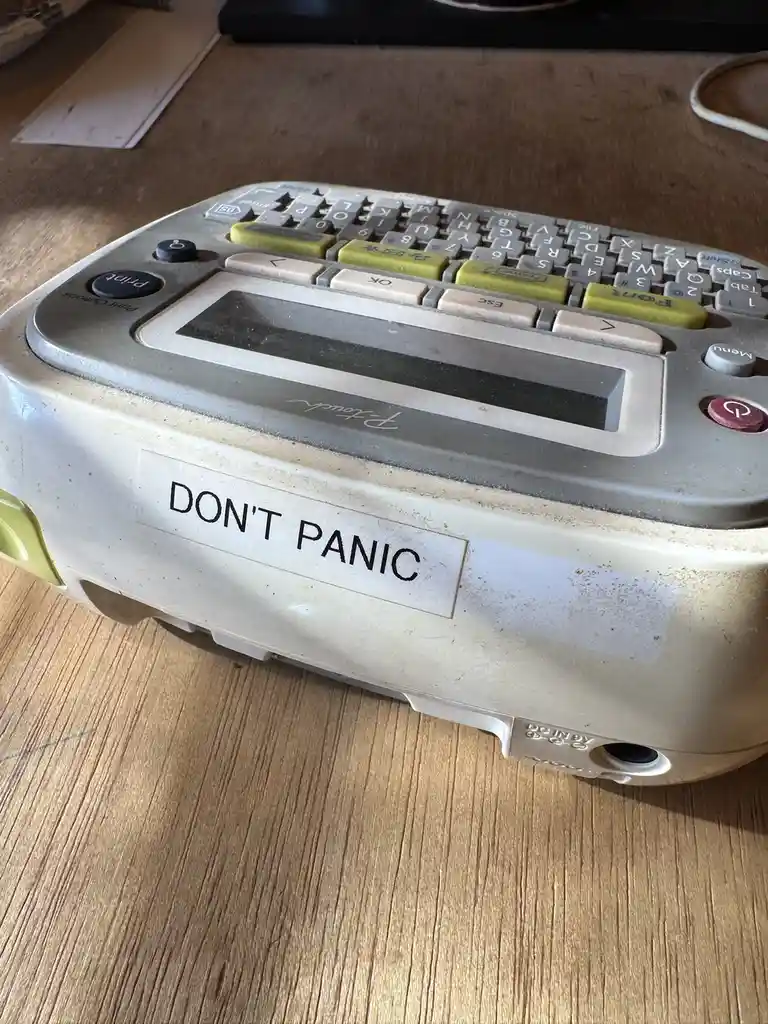 A close-up photo of a dusty, beige and green handheld electronic device, likely a P-touch label maker, sitting on a wooden…