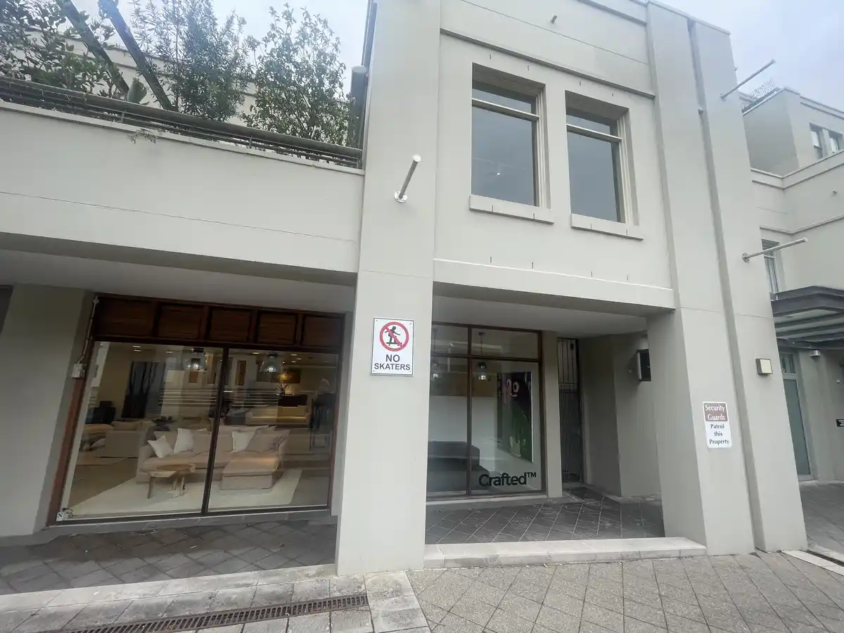 An exterior shot of a modern building with glass storefronts, one displaying 'Crafted™' and the other showing furniture…