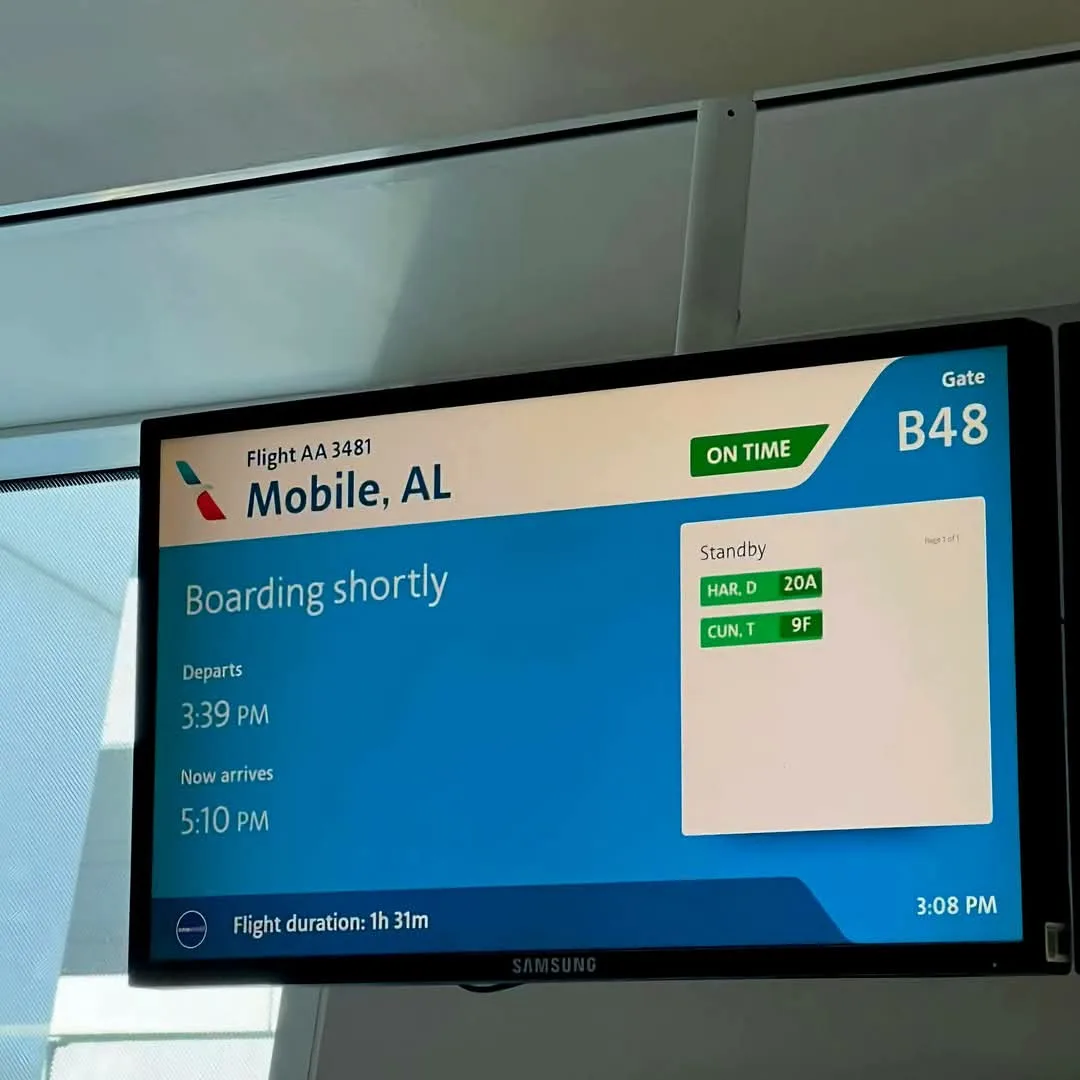 An airport gate screen for flight AA 3481 to Mobile, AL, shows 'Boarding shortly' with departure at 3:39 PM and arrival at…