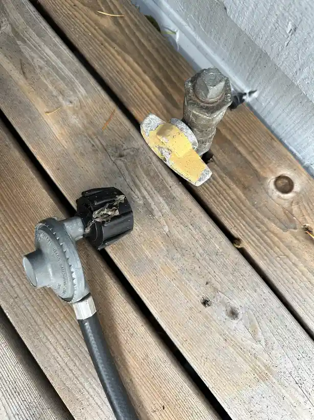 A close-up photo shows a weathered, yellow-painted metal valve handle and a black plastic hose connector lying on weathered…