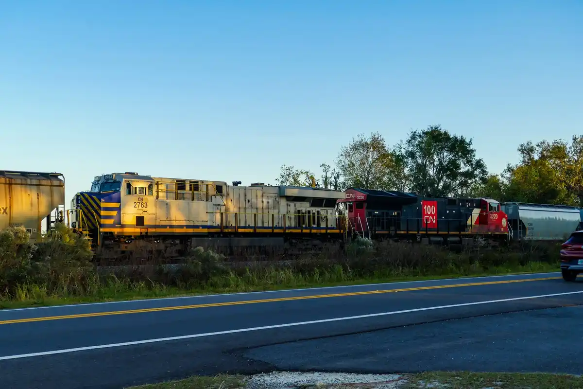 A photograph of two Canadian National Railway locomotives, numbered 2763 and 3220, parked on tracks beside a road with a red…
