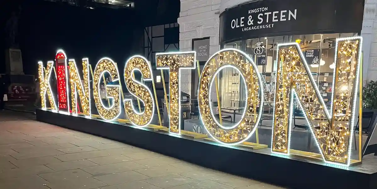 A nighttime photo shows large, illuminated letters spelling 'KINGSTON' with golden fairy lights and white LED outlines…