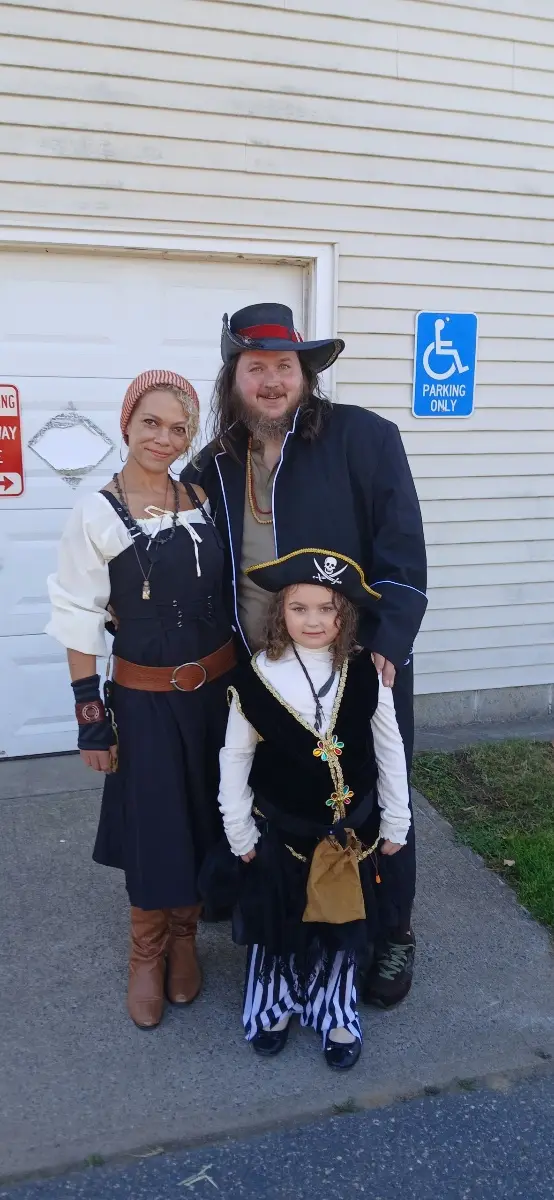 A family dressed as pirates poses for a photo in front of a house, with a blue 'parking only' sign featuring a wheelchair…