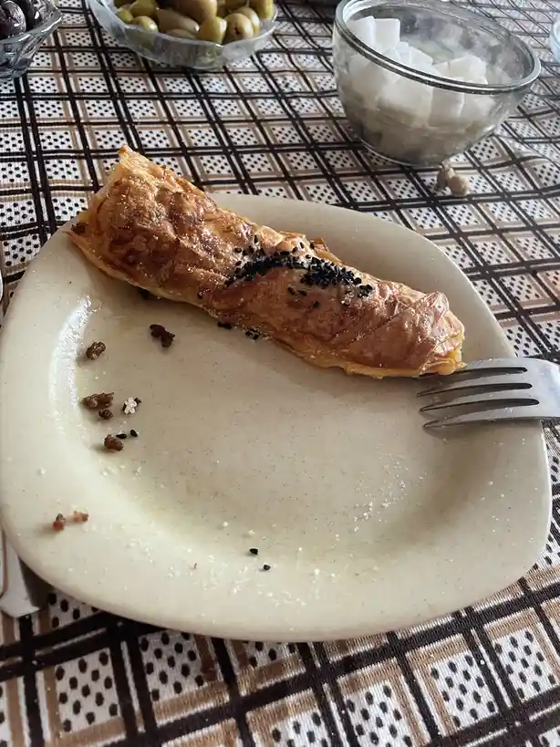 A partially eaten, golden-brown pastry with black sesame seeds sits on a beige plate, with crumbs scattered around and a…