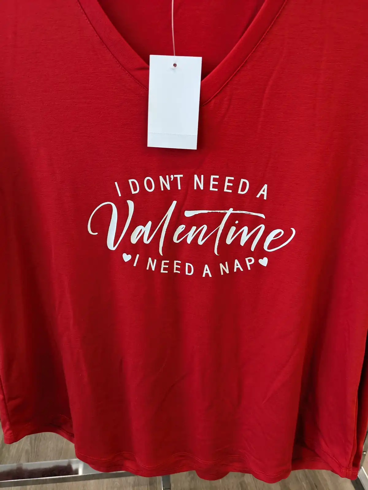 A red v-neck t-shirt with white text that reads 'I DON'T NEED A Valentine I NEED A NAP' with small hearts flanking the…