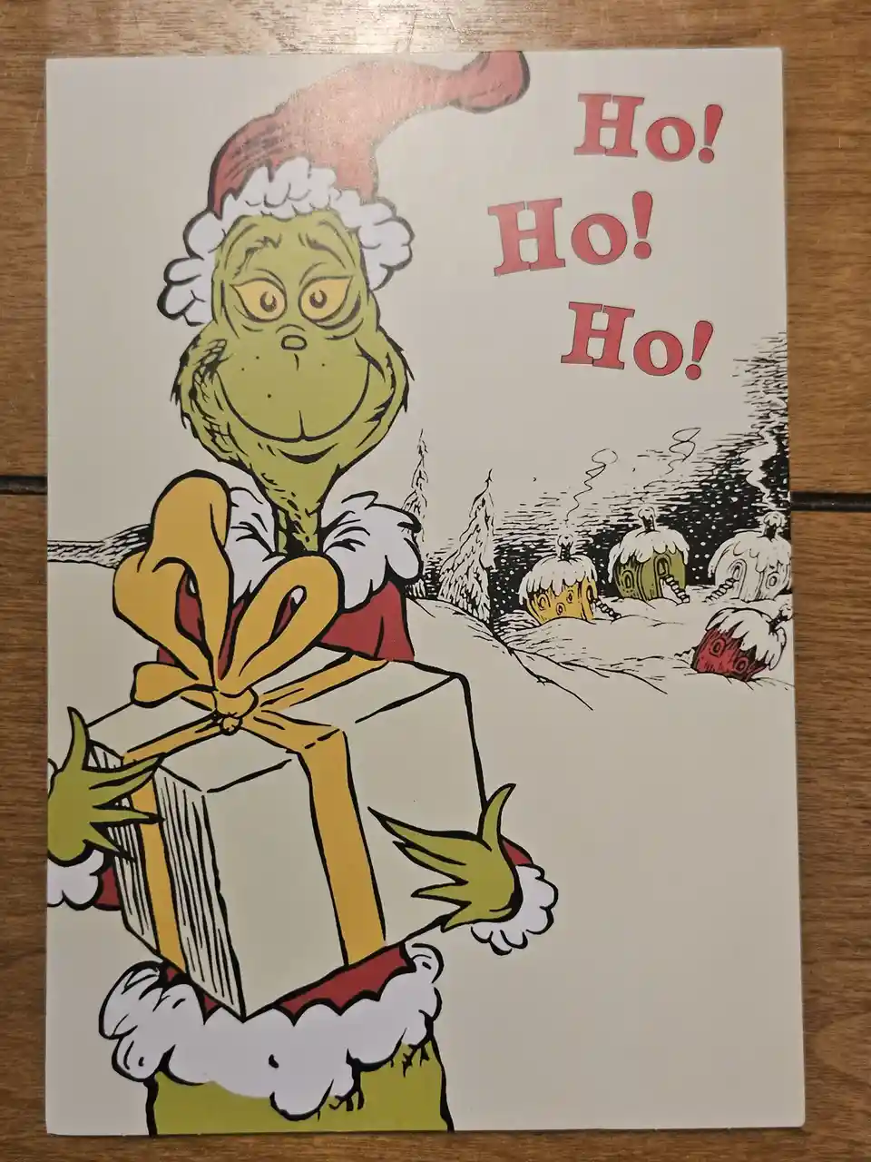 A classic Dr. Seuss-style illustration shows the Grinch wearing a Santa hat and holding a large gift wrapped with a yellow…