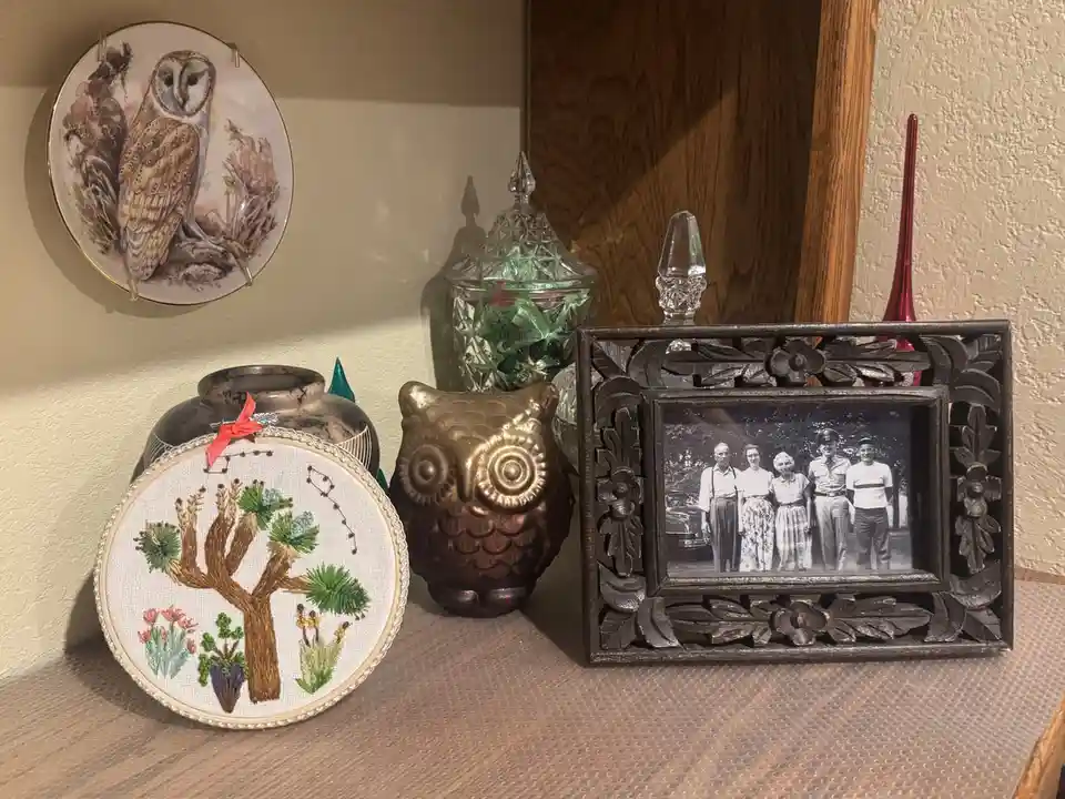A shelf displays various decorative items including a porcelain owl plate, a brass owl figurine, an embroidered tree hoop, a…
